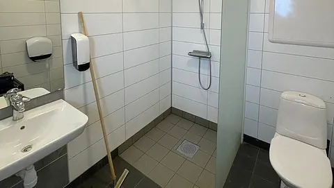 Lyst og moderne baderom med servant, dusj, toalett, såpedispenser og flislagt gulv og vegger.